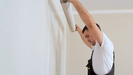 Worker attaching wallpaper to wall. One strip of new wallpaper wrapped in a roll.