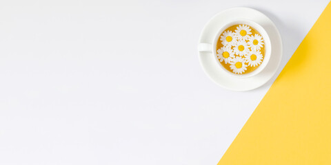 White chamomiles, cup of tea on yellow and white background. Herbal tea of chamomile flower. Chamomile tea concept. Flat lay, top view, copy space