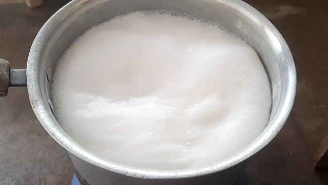 Milk boils and steams hot. Boiling milk in a stainless steel vessel. The milk is about to boil. Boiling milk flows from the pan onto the gas stove. Cow's milked boils in a kettle. 4K