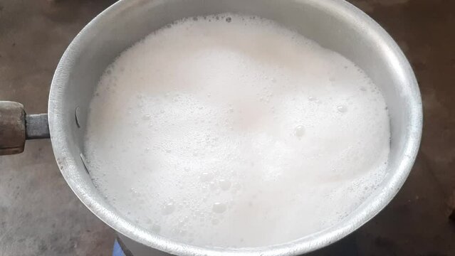 Milk boils and steams hot. Boiling milk in a stainless steel vessel. The milk is about to boil. Boiling milk flows from the pan onto the gas stove. Cow's milked boils in a kettle. 4K