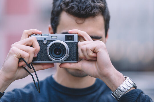 Young man capturing a moment with a vintage camera, focus on camera with blurred background