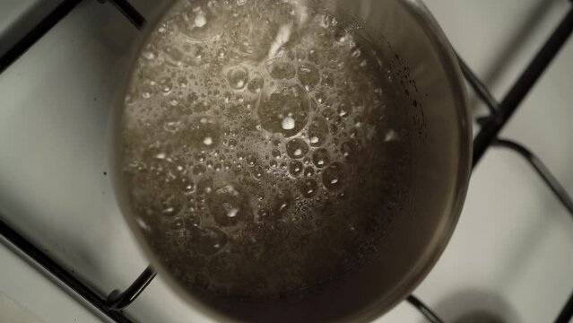 Boiling sugar syrup in a stainless steel pan on stove, top view. Boiling transparent sweet liquid in a metal container