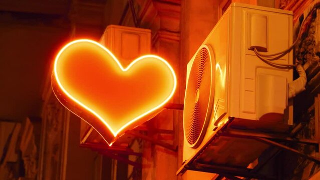 Bright red flashing heart on night street. There is an air conditioner and bright red flashing heart hanging on building in which there is sex shop. Air conditioning targets heart, cooling senses
