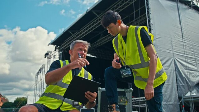 Male Production Team Moving Flight Cases And Setting Up Outdoor Stage For Music Festival 
