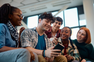 Multiracial group of happy students using cell phone in lecture hall.