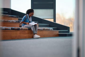 Black college student reading her lecture notes while learning at amphitheater.