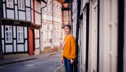 Fototapeta na wymiar Young Woman in a Bright Sweater Leaning on an Old Town Street