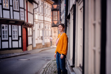 Fototapeta na wymiar Young Woman in a Bright Sweater Leaning on an Old Town Street
