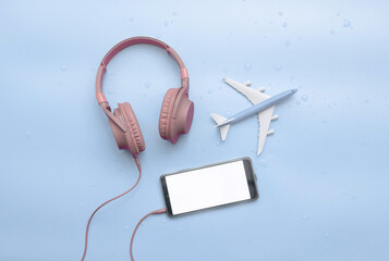 Top view, red musical headphones in water drops, with airplane travel concept, copy space. Headphones on a blue background on a wet surface on a blue background. Place for text. Background audio mp3.