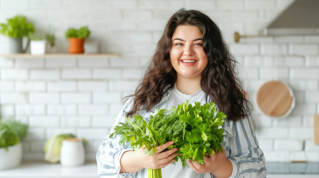 fat overweight smiling young woman with a bunch of greens on the background of a white kitchen, proper nutrition, salad, celery, weight loss, lifestyle, health, girl, food, cooking