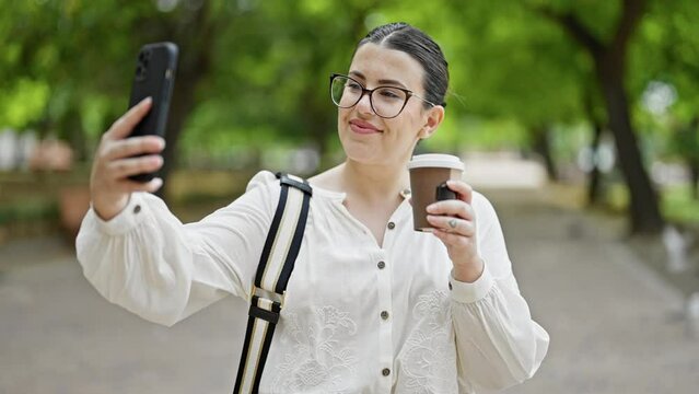 Young beautiful hispanic woman taking a selfie picture drinking take away coffee at the park