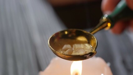 Female holding golden spoon with sticky liquid. Close up shot of woman warms wax in a golden old spoon on a candle for sealing stamp.
