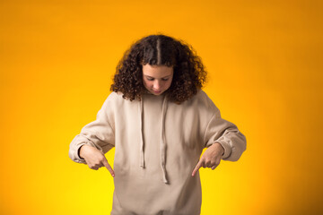 Girl pointing fingers down on yellow background. Advertisement concept
