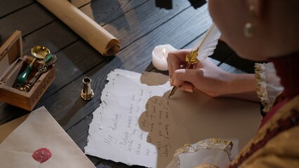 Female in antique outfit writes with feather pen. Over shoulder shot of woman writing a letter with...