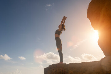 Woman standing on rocks by the sea doing a backbend, yoga pose.