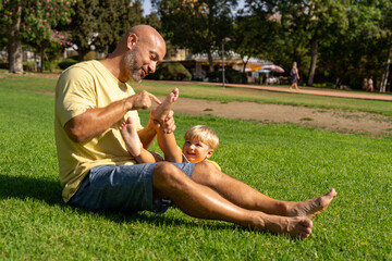 family and love concept - young father tickling his little son in park. dad tickles his son's legs...