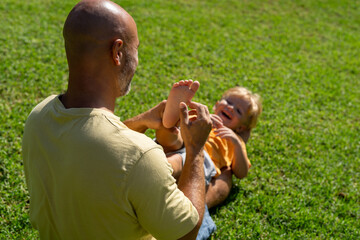 family and love concept - young father tickling his little son in park. dad tickles his son's legs...