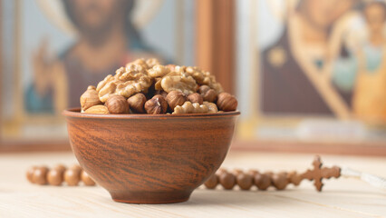 Various nuts in clay cup on table in front of Orthodox icon. Food for Christians during Lent,...