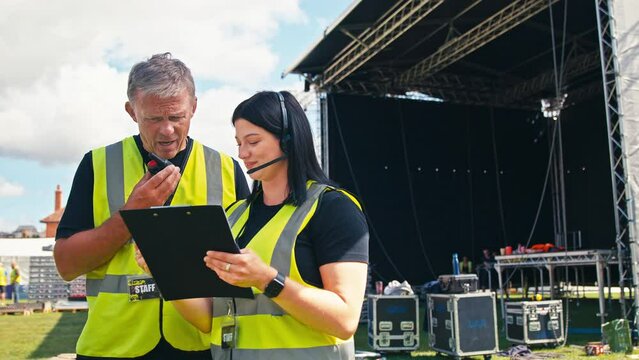 Production Team With Headsets And Clipboard Setting Up Outdoor Stage For Music Festival Or Concert
