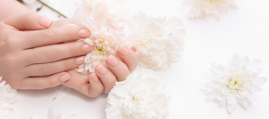 Concept cosmetic cream and beauty health care. Stylish trendy nail young woman hands pink manicure on white background with flowers, top view