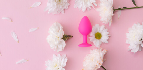 Top view Sex toy plug on pink background with flowers, copy space
