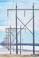 Row of tall wooden transmission towers with electrical lines providing power to customers along a Western province portrait view.