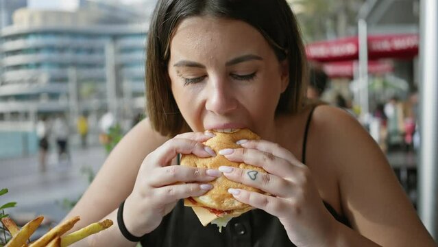 A young woman enjoys a burger and fries at an outdoor street cafe in a casual urban setting.