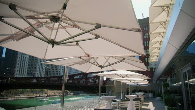 A row of white umbrellas are sitting on a patio next to a river. Move camera