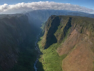 Green Grass Covered Canyon Floor with River Tall Cliff Sides Cloudy Blue Sky