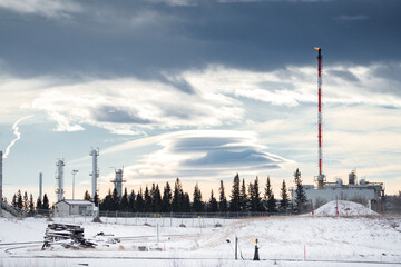 Oil and gas plant with a flare stack and flame under a dramatic winter sky in Western Canada.