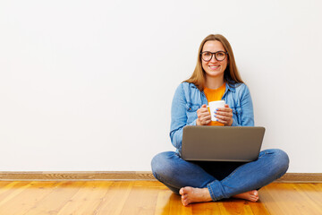 Content Woman with Laptop and Coffee Mug Sitting on Floor