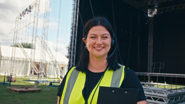 Portrait Of Female Production Worker With Radio Headset Setting Up Outdoor Stage For Music Festival 