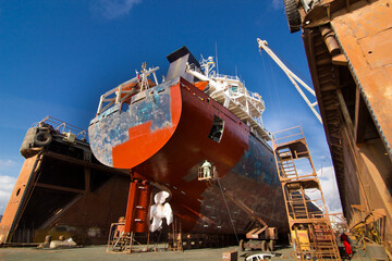 Commercial vessel undergoes maintenance in floating dock. Workers paint, repair hull, under clear...