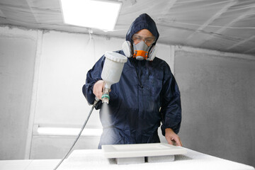 Application white color on facade kitchen furniture, spraying device. Painter staining wood with spray gun