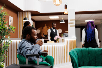African American businessman drinking coffee while waiting for check-in procedure in hotel lobby....