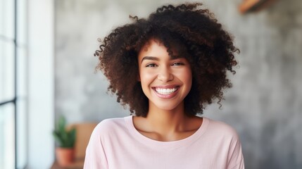 Fototapeta premium Indoor portrait of beautiful brunette young dark-skinned woman with shaggy hairstyle smiling cheerfully, showing her white teeth to camera