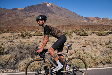 Obraz premium Man cyclist pedaling on road with view on mountain Teide volcano,Tenerife,Canary Islands,Spain. Sportsman training hard on bicycle outdoors.Sport motivation.Cycling training outdoors.Hipster cyclist.