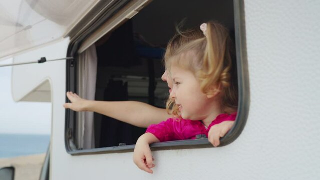 Cheerful mother and daughter look out of the camper window at nature. Family holidays