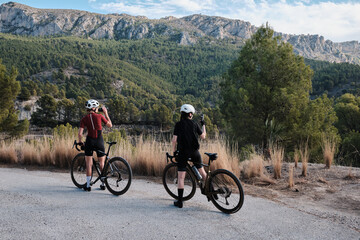 Fototapeta premium Two professional women cyclists riding gravel bicycles on a gravel road on a sunny summer day. Group bike ride in the natural countryside. Gravel advanture. Gravel cycling adventure. Alicante, Spain .
