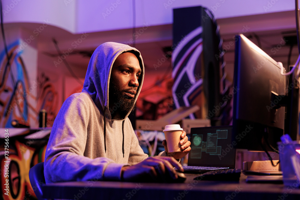 Poster hacker drinking coffee to go while doing criminal activity on computer late. african american man ha
