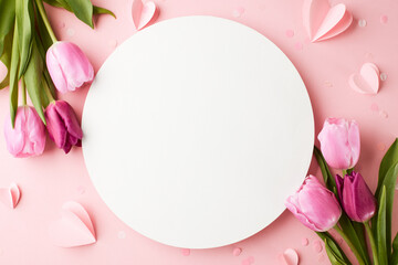 Blank canvas of spring: blooms and wishes. Top view flat lay of pink tulips and paper hearts on a pastel pink background with blank circle for heartfelt spring messages