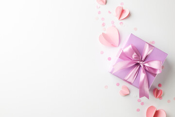 Cherished surprises: delicate choices for her special day. Top view shot of a lavender gift box tied with a satin pink ribbon, paper hearts on a white background with space for advertisements