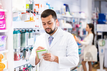 Friendly man pharmacist standing at drugstore with notepad and pen in hands