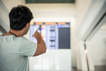Traveler man photographed from behind pointing to the terminal timetable