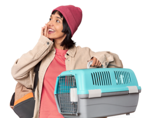 Young Hispanic woman ready for travel with pet carrier touching back of head, thinking and making a choice.