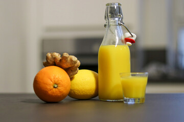 Close up of homemade orange, lemon and ginger drink in a glass bottle with a small shot glass
