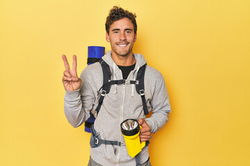 Hiker with backpack and lantern on yellow showing number two with fingers. - obrazy, fototapety, plakaty