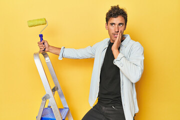 Man with ladder and paint roller on yellow is saying a secret hot braking news and looking aside - Powered by Adobe