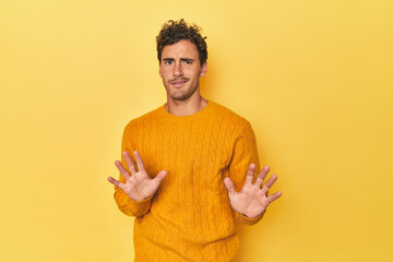 Young Latino man posing on yellow background rejecting someone showing a gesture of disgust.