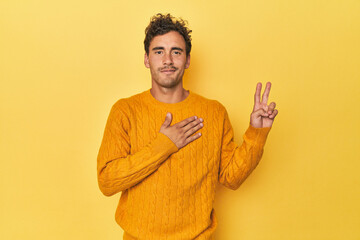 Young Latino man posing on yellow background taking an oath, putting hand on chest.